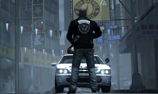 A member of The Lost biker club seen from behind, leather jacket with the gang's patch, standing in the rain in front of a police car with its headlights on in a Chinatown street in Liberty City