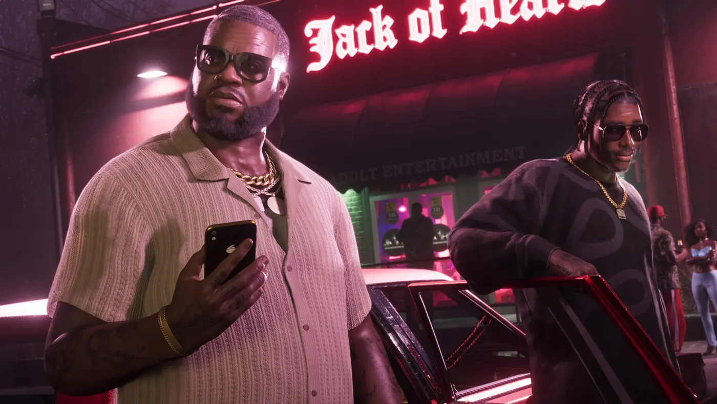 Night scene in GTA VI: a heavyset man in a light shirt and gold chain holds a smartphone outside a club lit by a red neon 'Jack of Hearts' sign reading Adult Entertainment, while a second character in dark sunglasses leans on the door of a dark car